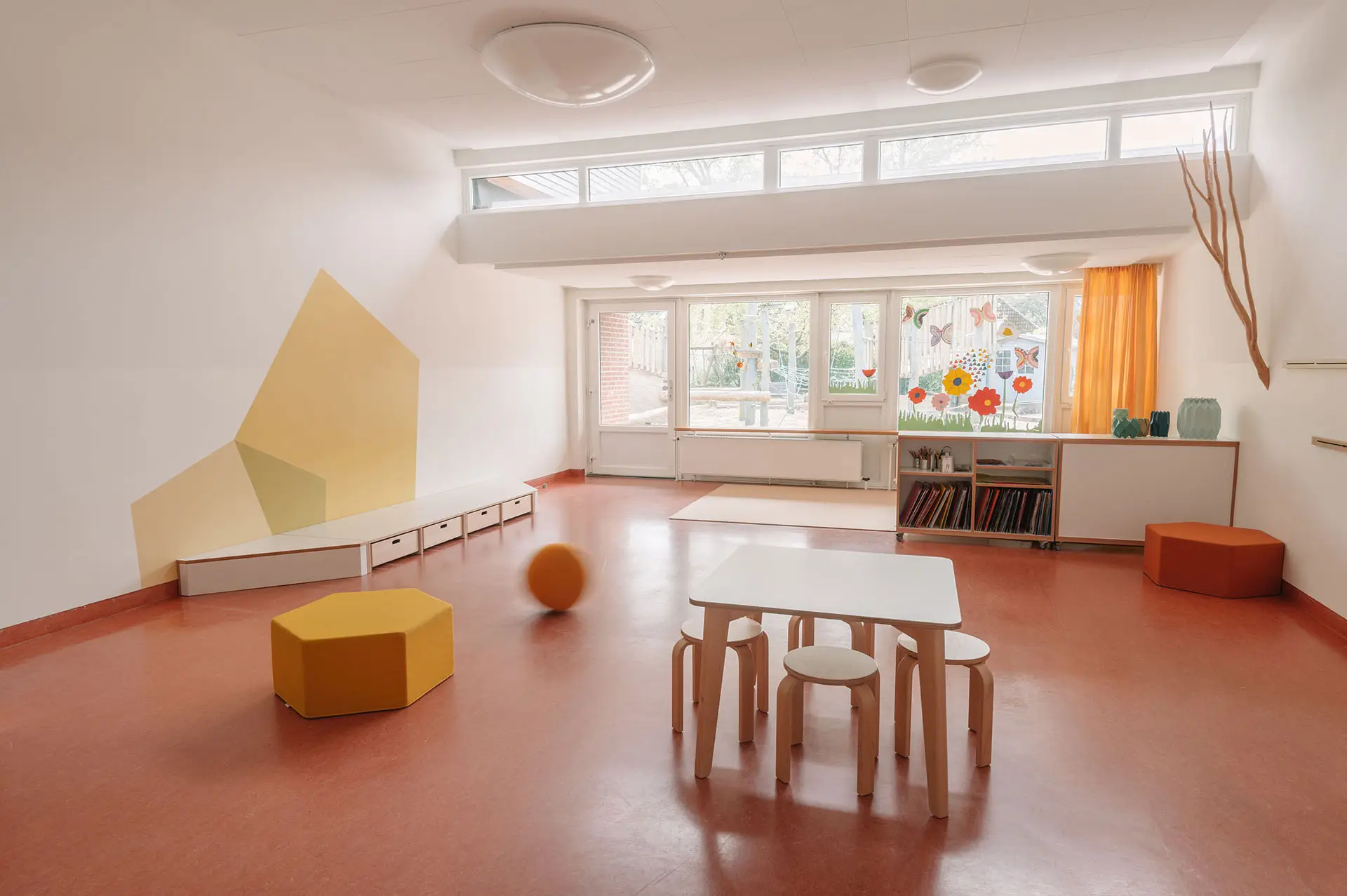 Kindergartenmöbel und Raumgestaltung von papoq: Bewegungsraum einer Kita mit einem Kind, das auf Kletterbäumen klettert, während Sicherheit durch einen Fallschutz gewährleistet ist.