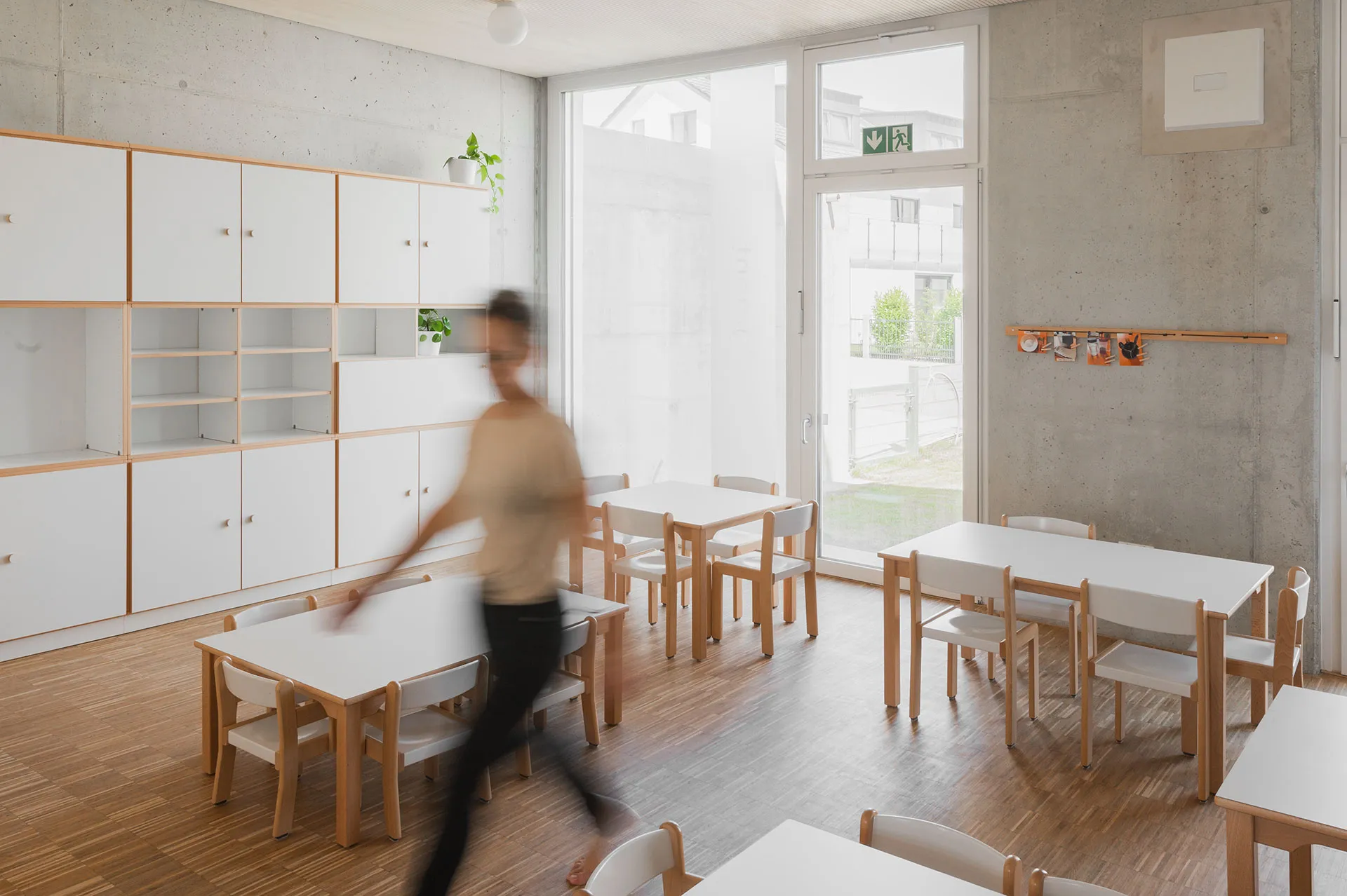 Kindergartenmöbel und Raumgestaltung von papoq: Bewegungsraum einer Kita mit einem Kind, das auf Kletterbäumen klettert, während Sicherheit durch einen Fallschutz gewährleistet ist.