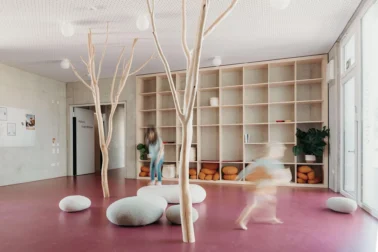 Eingangsbereich mit Wildholzbäumen und Filzsteinen Kindergartenmöbel und Raumgestaltung: Kinder spielen im Eingangsbereich der Kita mit Filzsteinen, umgeben von Dekobäumen aus echtem Wildholz, die eine einladende Atmosphäre schaffen und die Eingewöhnung erleichtern.