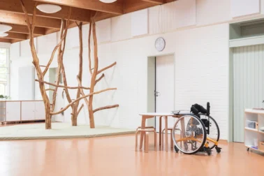 Inklusive Kita Inklusive Kindergartenmöbel von papoq: Rollstuhl am Tisch neben Kletterbäumen mit Fallschutz, fördert barrierefreies Spielen und Lernen in der Kita.