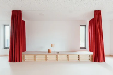 Theaterbühne und Matratzenpodest Kita Papoq Matratzenpodest für Kindergärten: Vielseitig nutzbares Podest mit roten Vorhängen für Theater und Rückzugsort, integrierte Schubfächer bieten Stauraum, robust und kindgerecht.